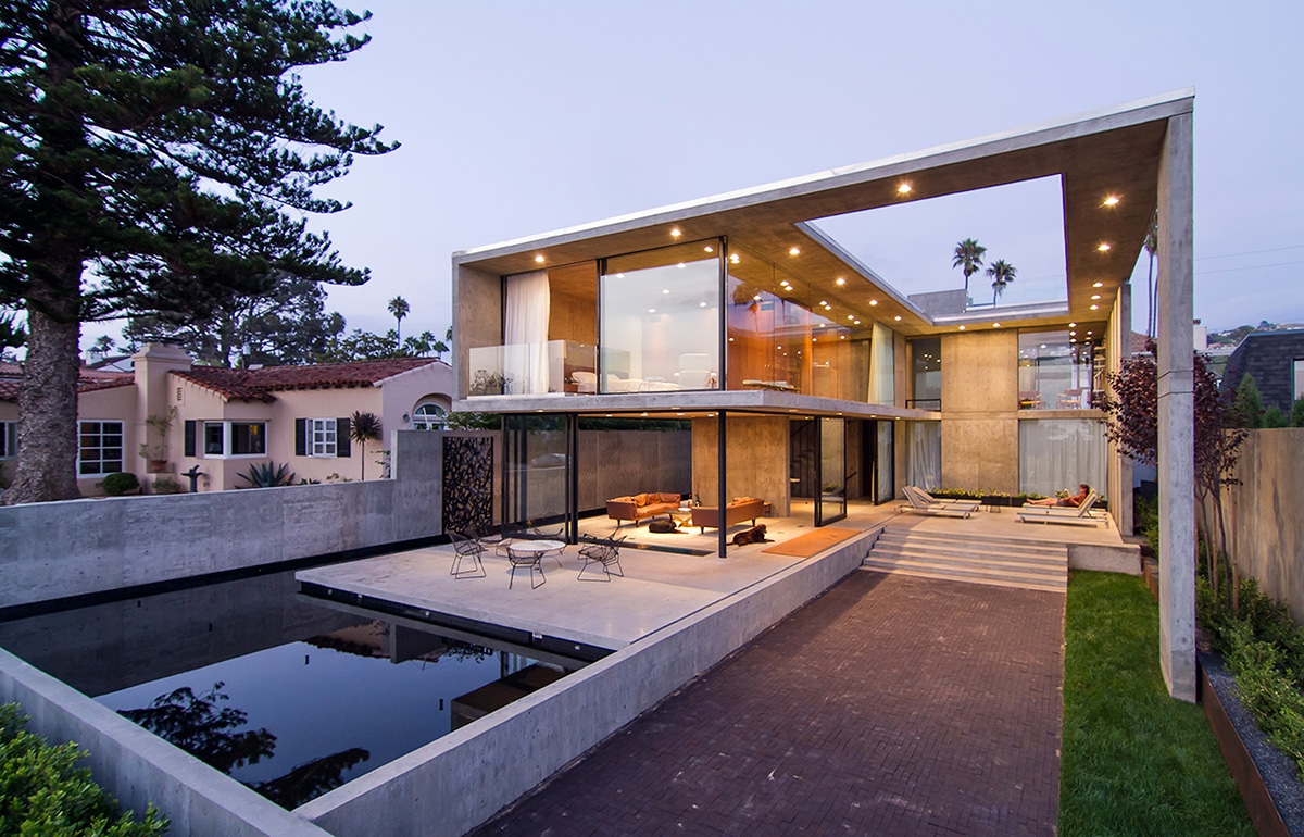 The front view of a two-story home with almost entirely glass walls encasing the concrete home.