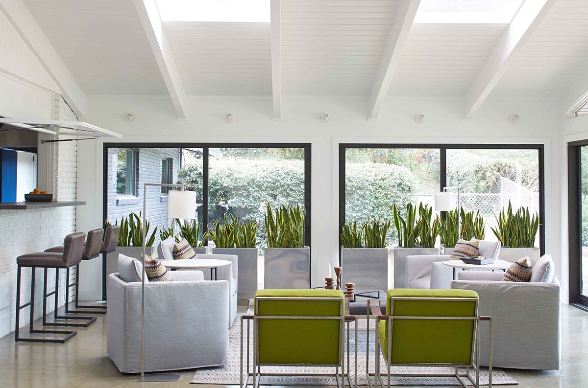 The enclosed sunroom allows views to the outdoors through large sliding glass doors behind sansevieria plants.