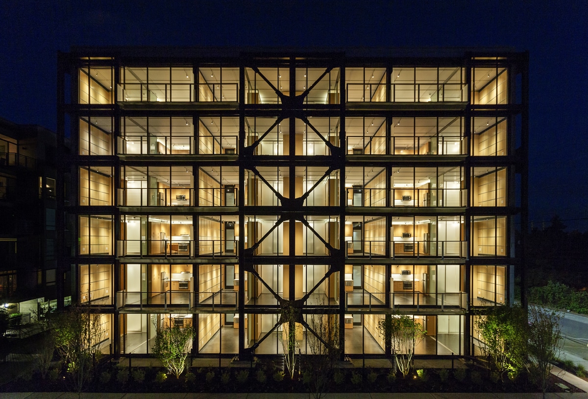 A nighttime view of the multi-family building with walls of glass on every floor.