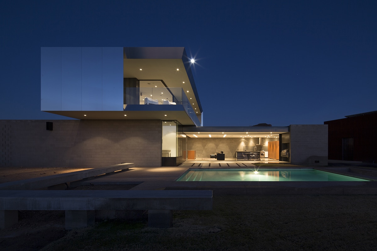A view of the two-story, concrete and glass home that completely opens to the landscape through wall-to-ceiling multi-slide doors.