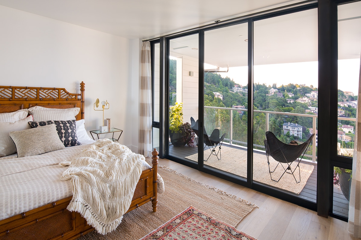 A large sliding glass door connects this bedroom to a balcony overlooking the green neighborhood below.