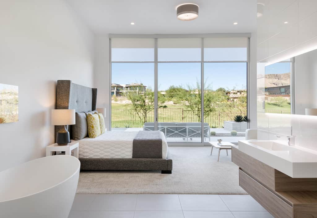Shades of White’s large moving walls of glass flood interior spaces with natural light, like in this bedroom connected to an open concept bathroom.