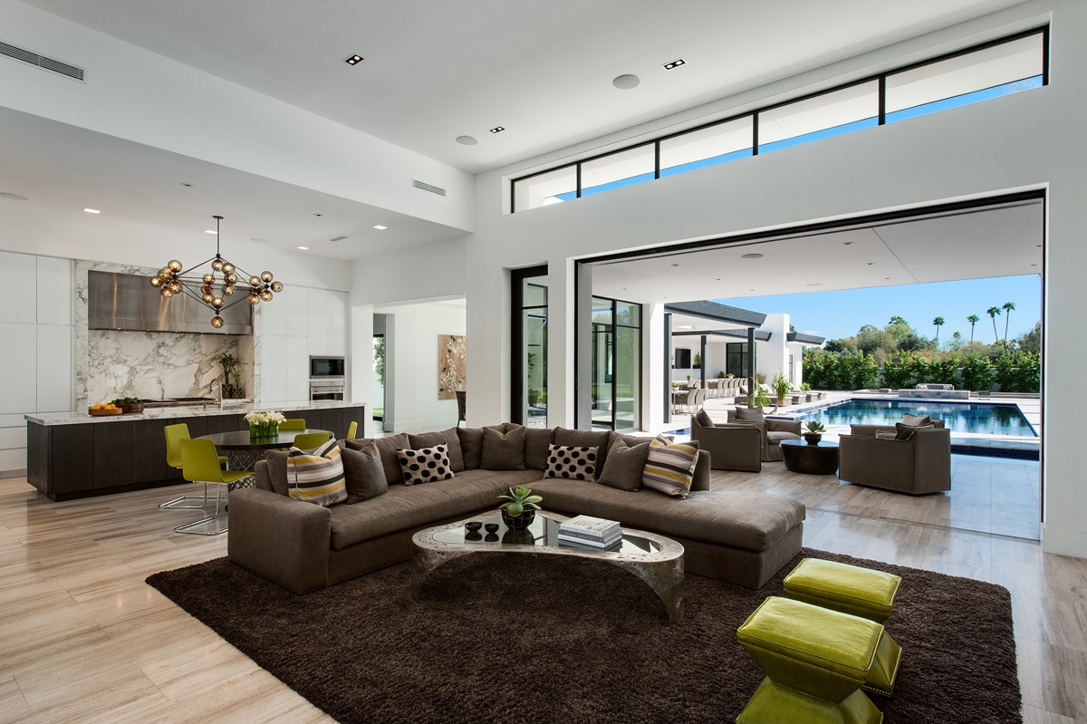 A pocketing multi-slide door seamlessly merges the great room, decorated with brown furniture and green accents, with the expansive pool area in the backyard.