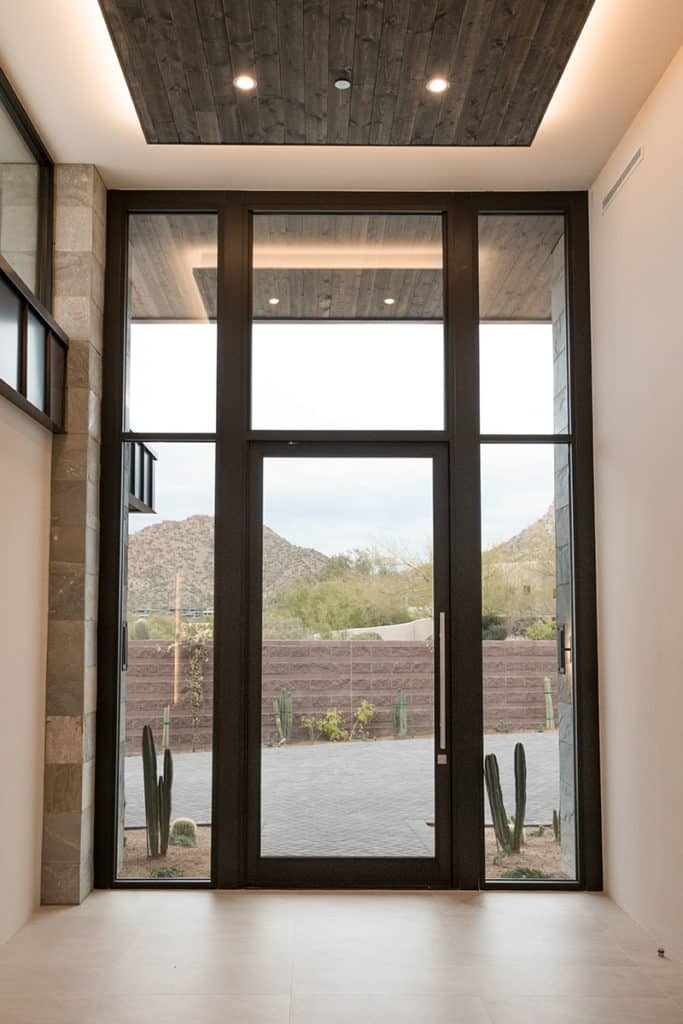 A glass pivot door encased by glass panels provides a dramatic entrance into the home.