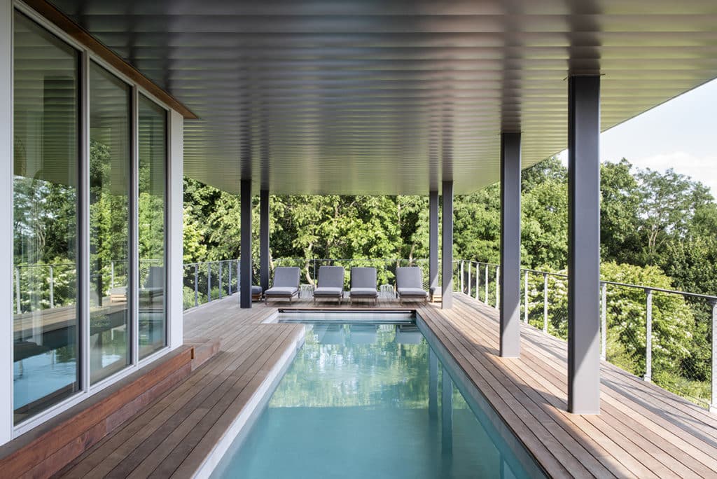 Sliding patio doors open to a covered outdoor deck with a pool and a view of trees.