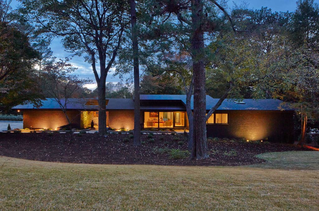 An outside view of the Midcentury Modern home with views to the living room through glass doors.
