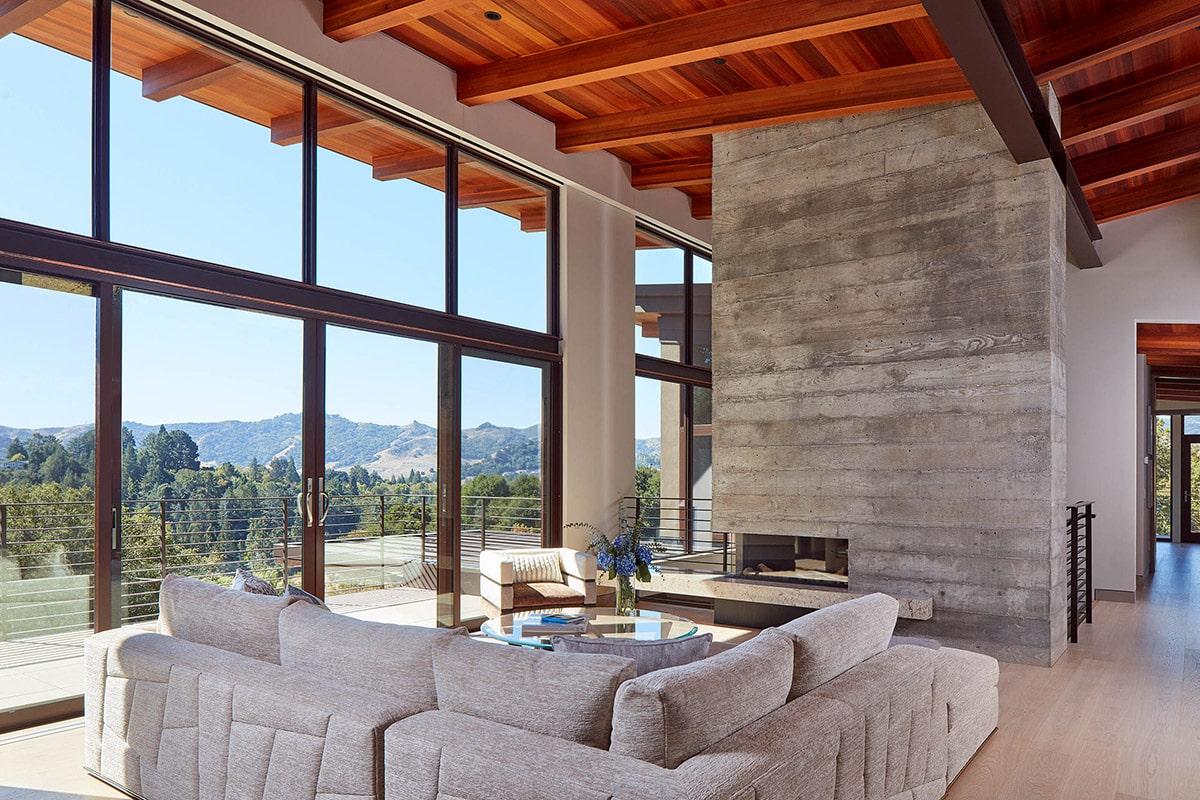 A collection of fixed windows and sliding glass doors connects the living room to a deck with hillside views.