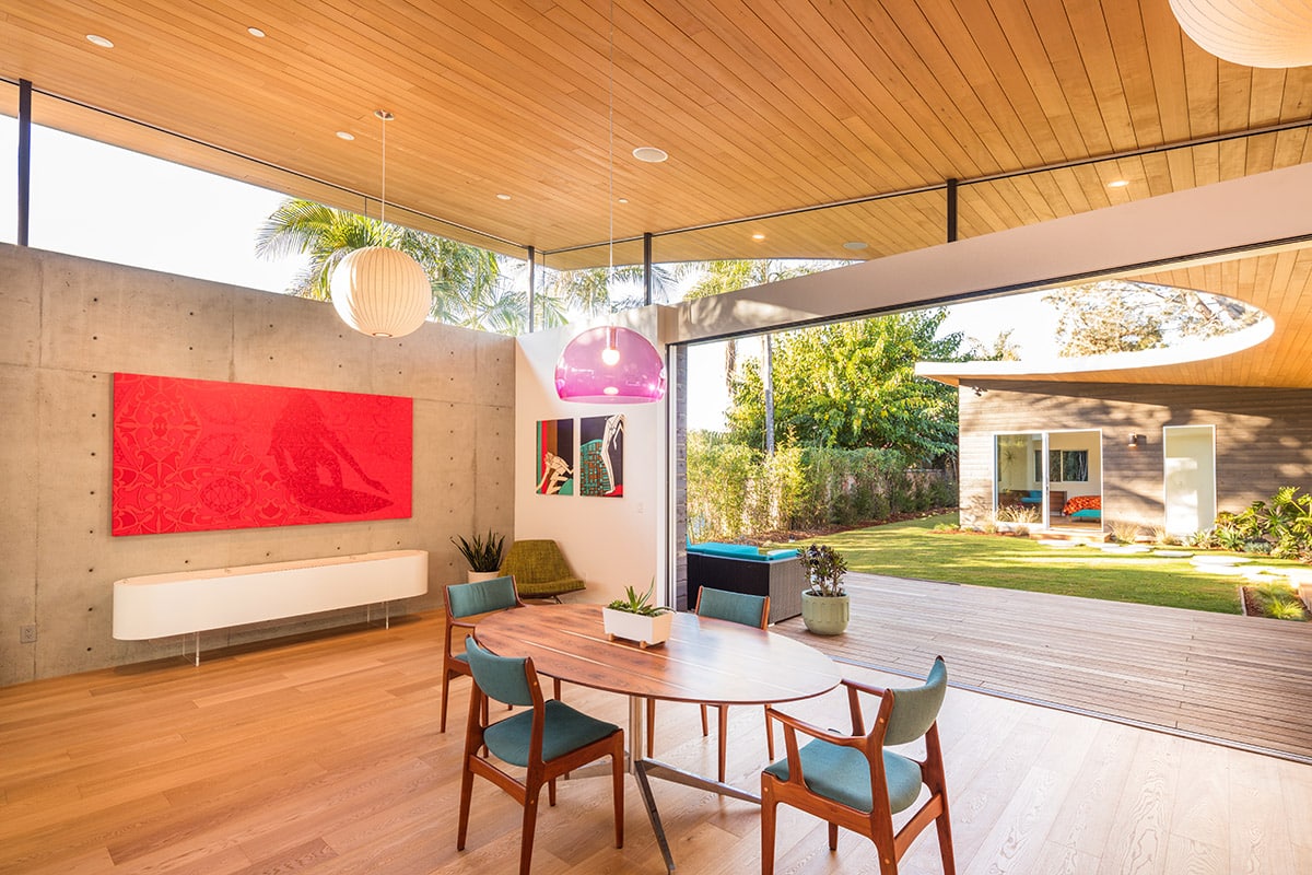 A modern home dining area opens to a backyard patio through a large, multi-slide glass door.