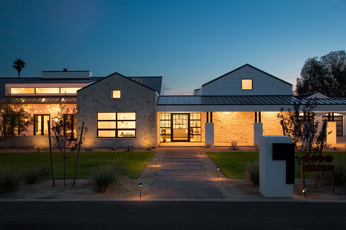 This desert home uses large panels of glass, like in this view of the front of the farmhouse-style home, to connect to nature while keeping the heat out.