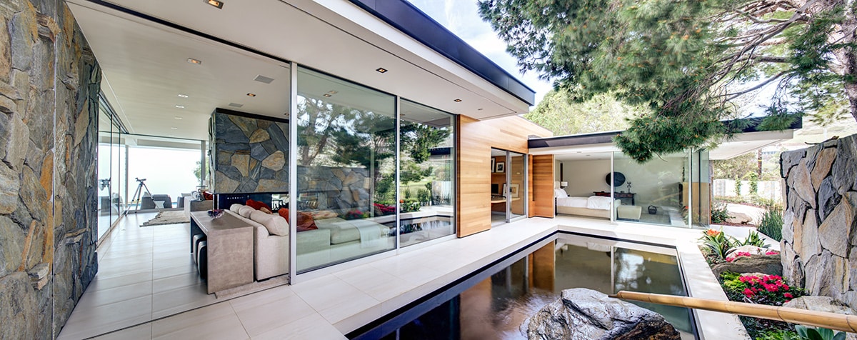 The open sliding glass doors connect indoor spaces to the courtyard with a man-made pond.