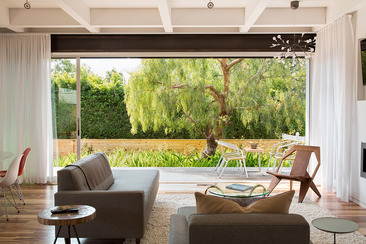 The multi-slide door creates a seamless transition between the living room and the green outdoor area of the home.