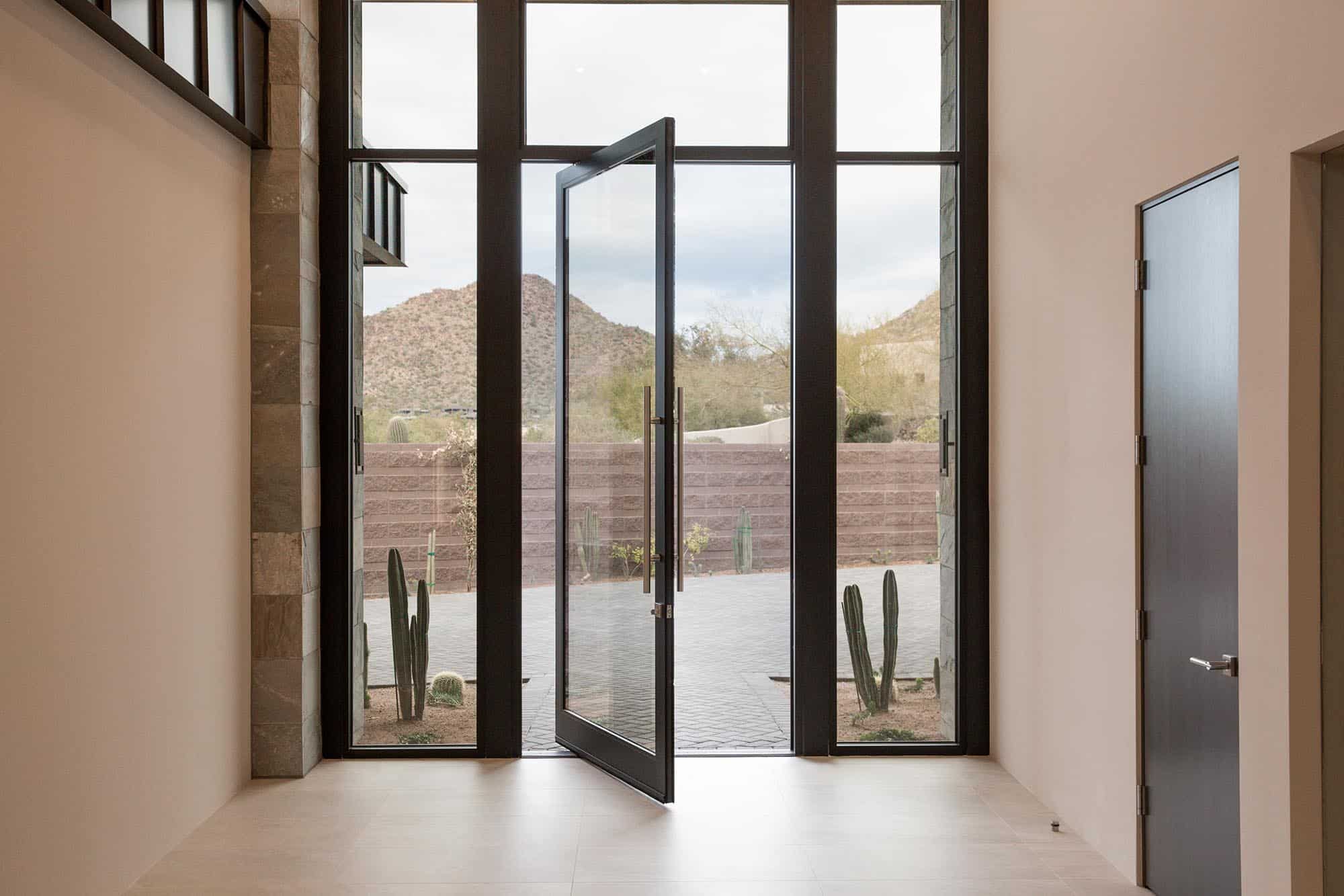 A large pivot door surrounded by glass panes opens the entryway to the desert.