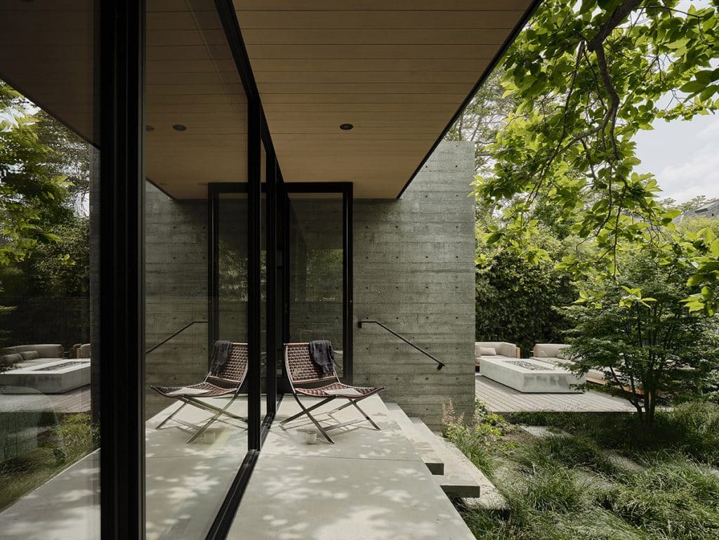 The master bedroom connects to the backyard through a glass wall, framing the green landscape full of trees.