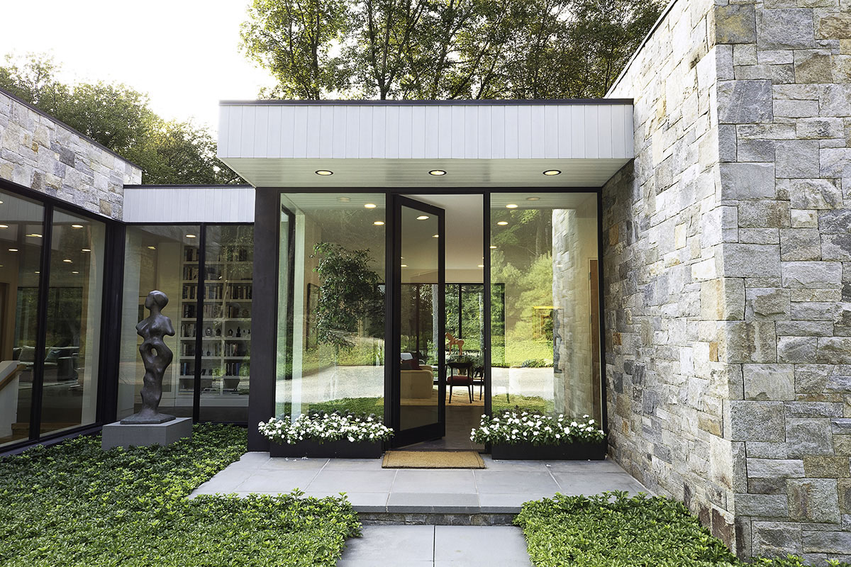 A tall pivot door greets guests as they enter the glass encased abode that frames art and nature together.