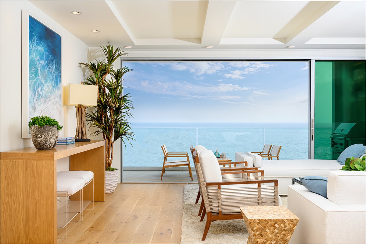 A fully opened multi-slide door connects the livening room with the balcony and frames views of the ocean.