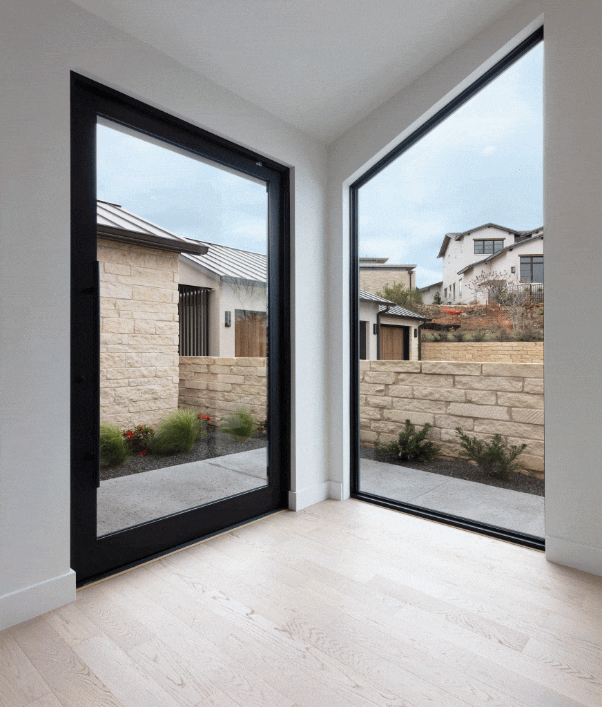 A massive pivot door, mirrored by a fixed window, provides a seamless indoor-outdoor connection.