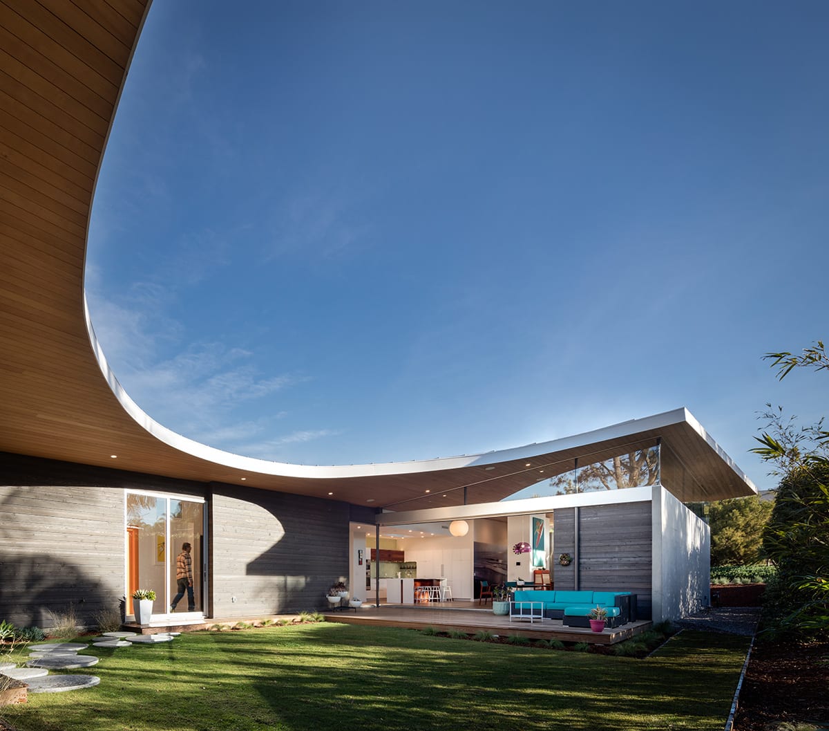 The home's wood-paneled curvilinear roof provides a unique profile as it leaves the grassy backyard uncovered.