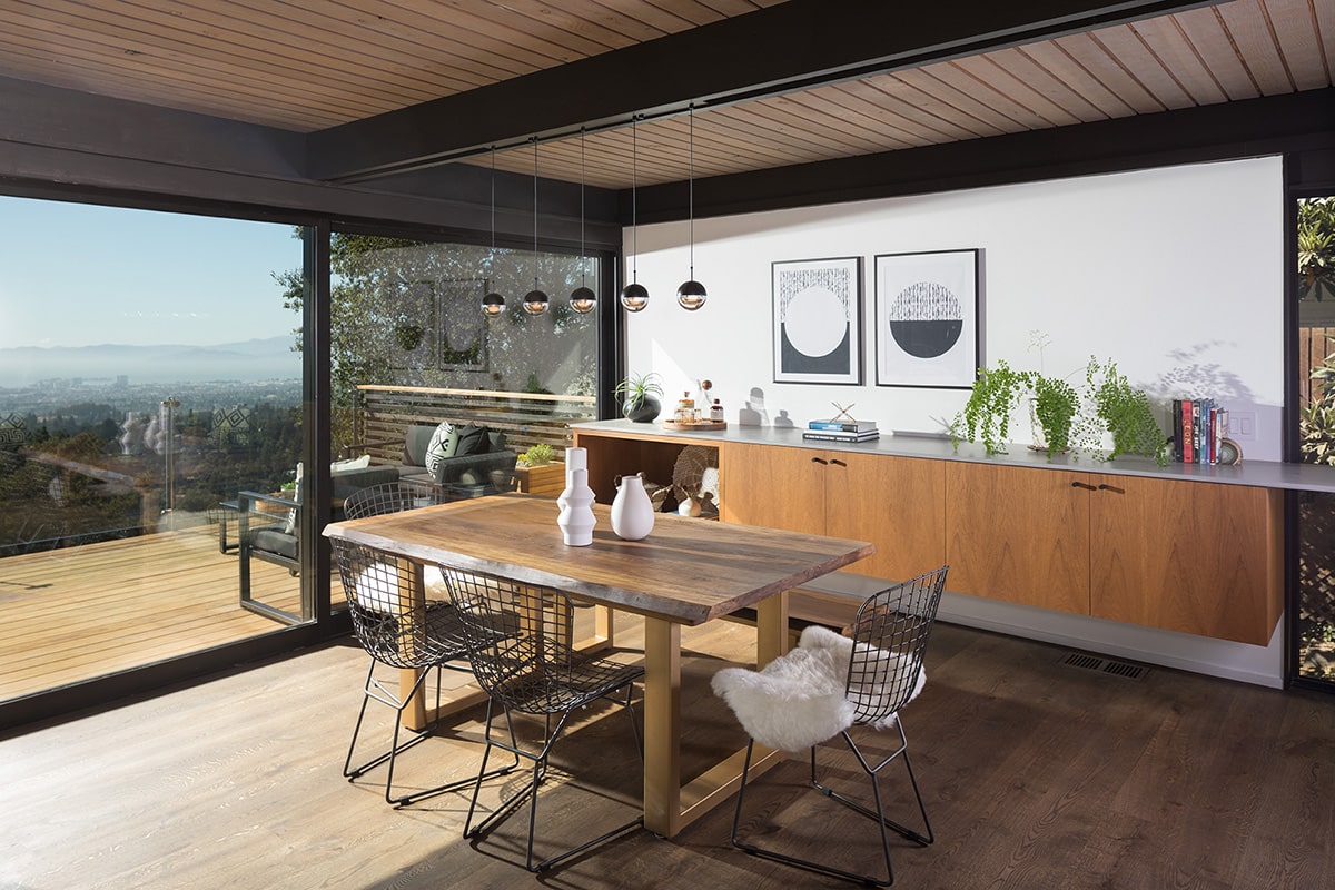 The dining area’s indoor-outdoor connection is bolstered by wood accents and massive sliding glass doors that open an entire wall to the balcony.