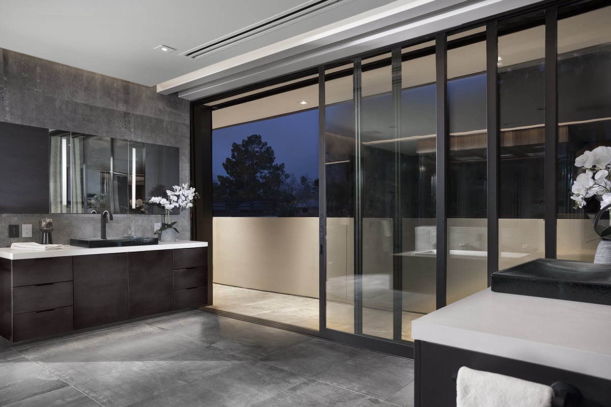 The floor-to-ceiling multi-slide system completely opens the large bathroom to the walkway outside, which has a partial wall that allows for privacy.