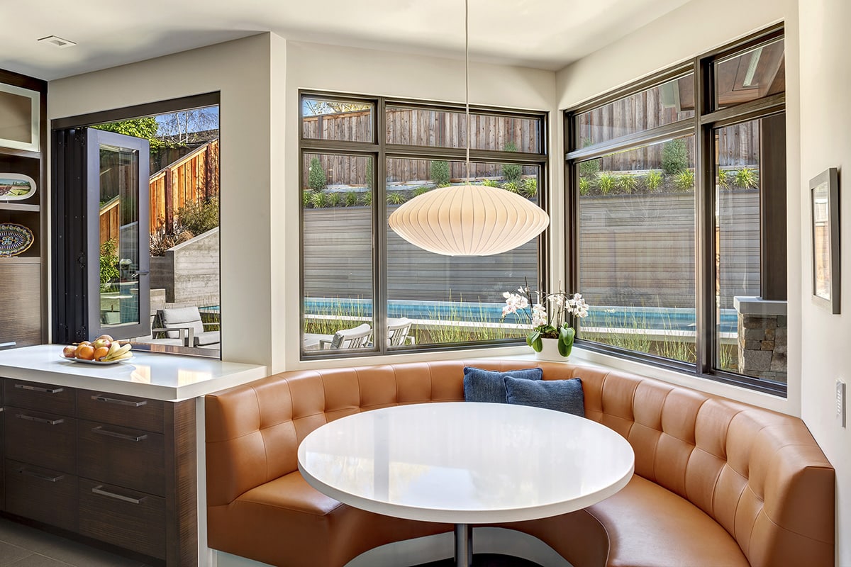 A bi-fold window connects the backyard to the kitchen while a breakfast nook in the corner is bathed in light from fixed windows.