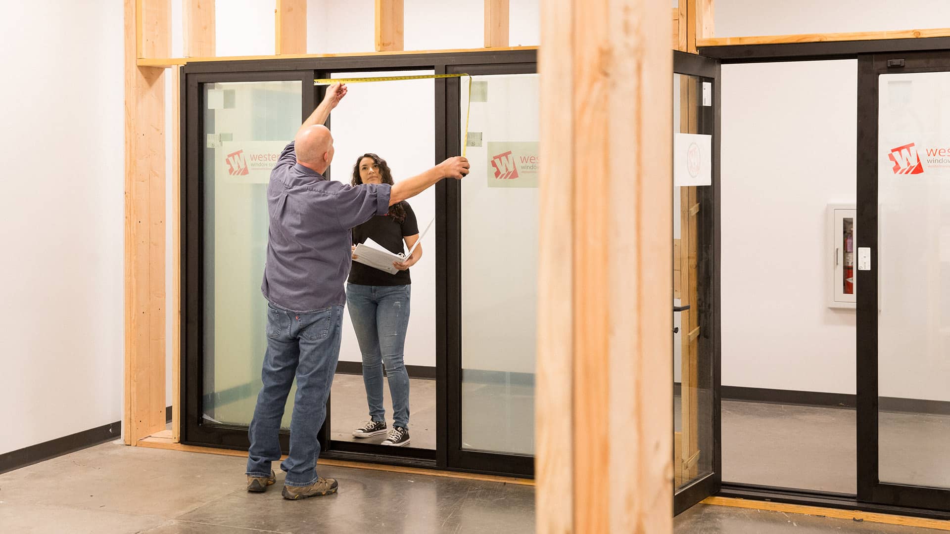 Two employees measure an installed sliding door panel.