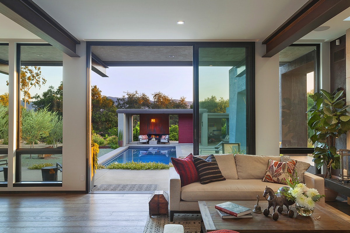 The open multi-slide allows direct access to the pool in the backyard from the living room, while the floor-to-ceiling windows on either side contribute to the flood of natural light.