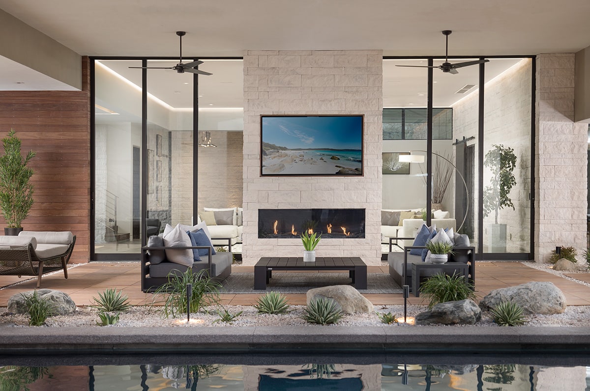 Two multi-slide doors border an outdoor fireplace and mounted TV, creating open airflow between the indoor and outdoor seating areas.