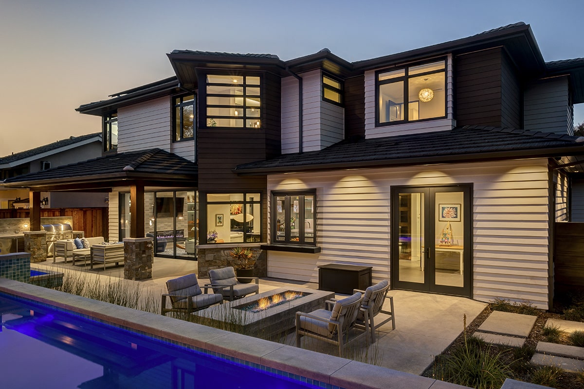 A backyard view of the contemporary-meets-Craftsman design that features an attractive outdoor living space equipped with a pool, firepit, and two seating areas.