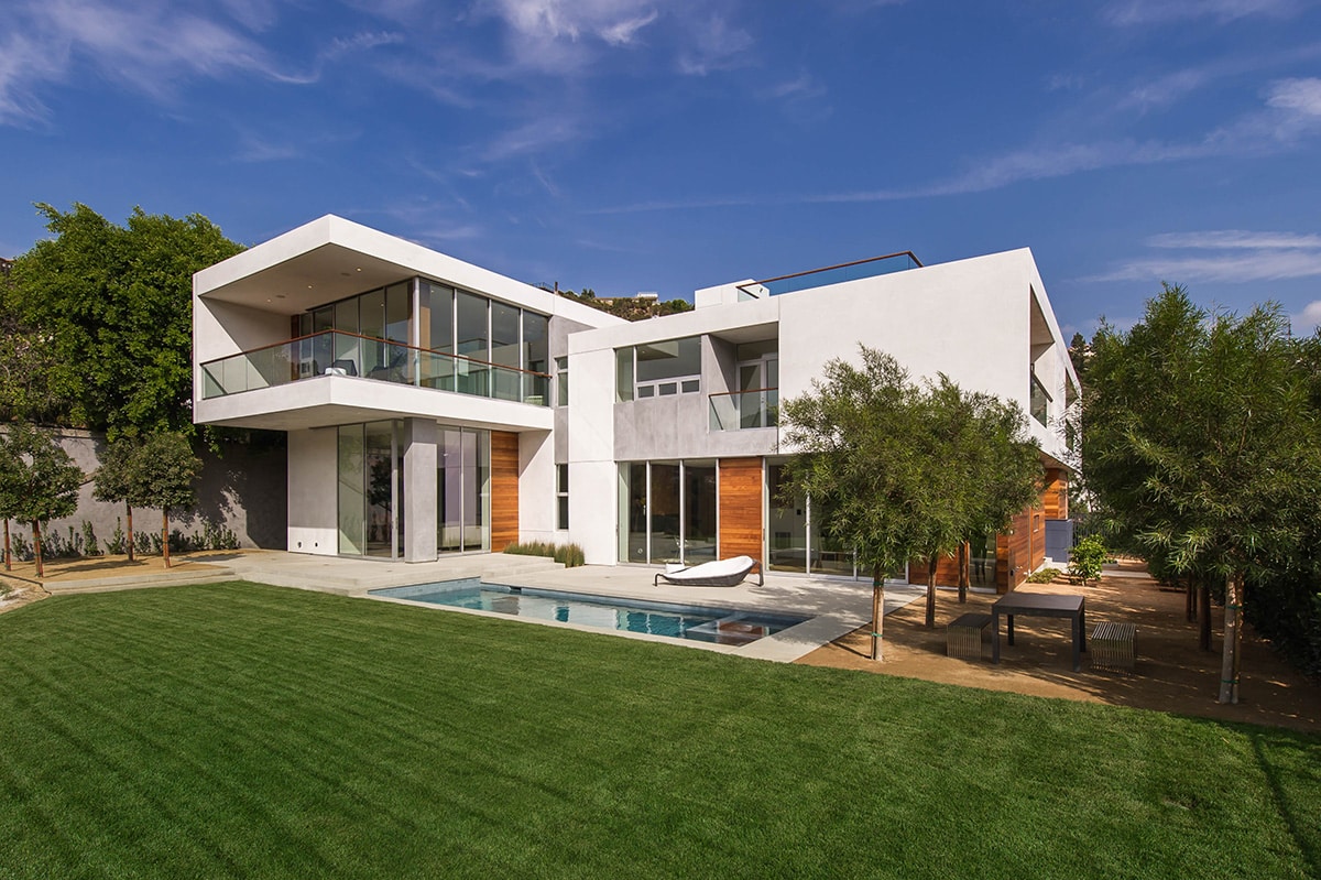 A view of a two story home with wall-to-ceiling multi-slide doors that connect rooms to balconies and the backyard.