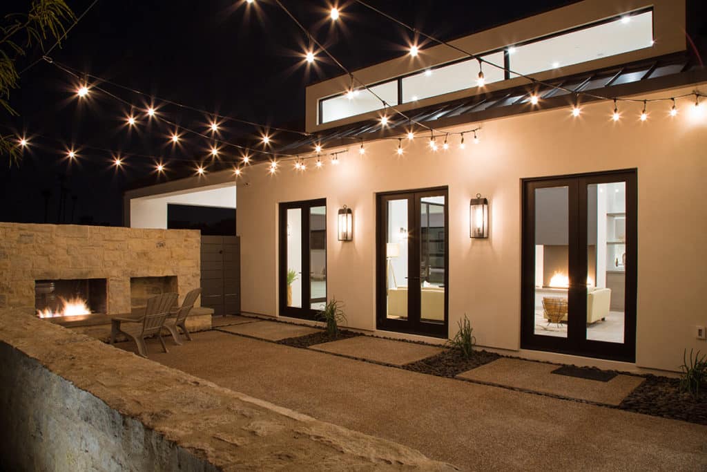 Three glass double doors open to a front-yard patio with a fireplace.