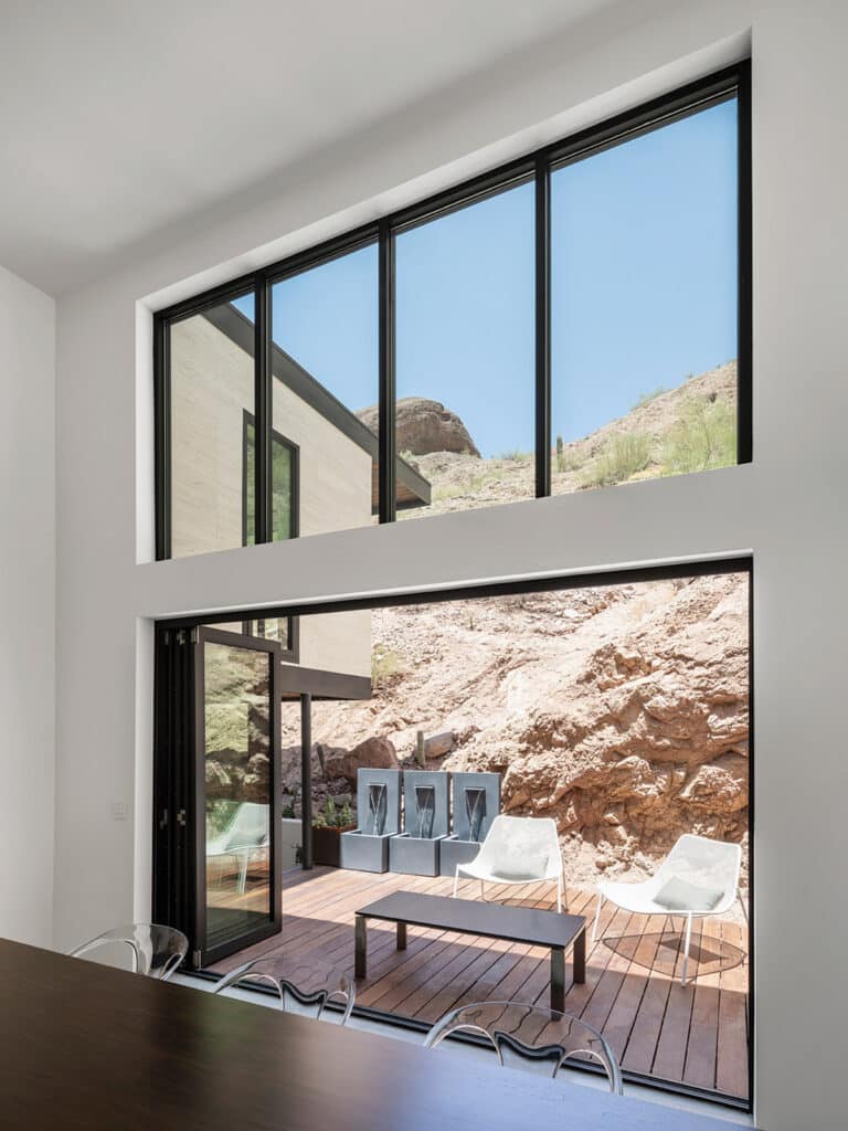An open bi-fold door connects the dining area to an outdoor seating area right by mountainous terrain.