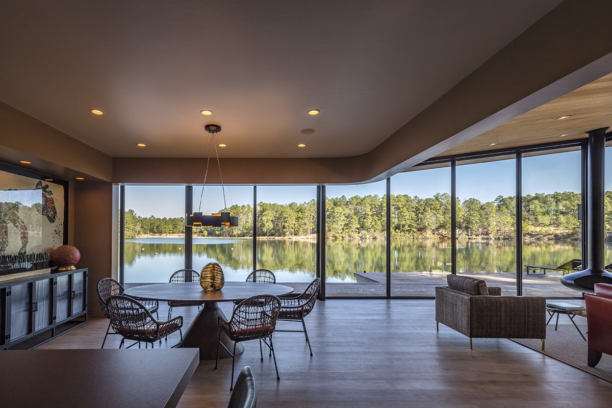 A dining room and living area share glass walls that allow views to the lake outside.