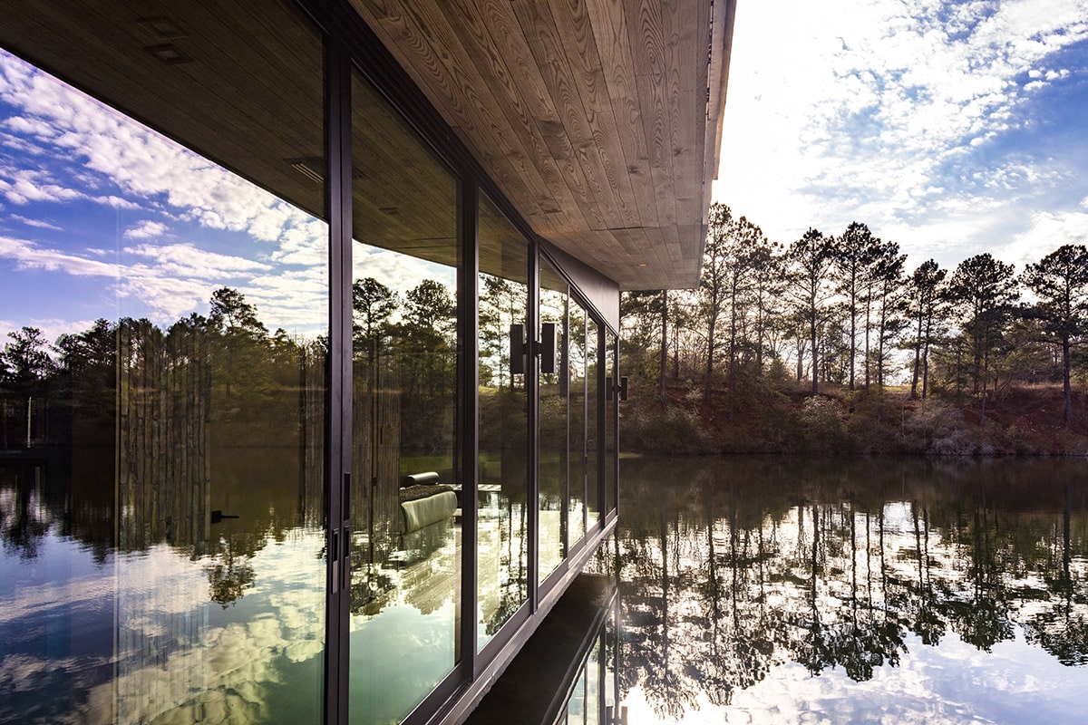 A home’s glass exterior reflects the surrounding woods and trees.