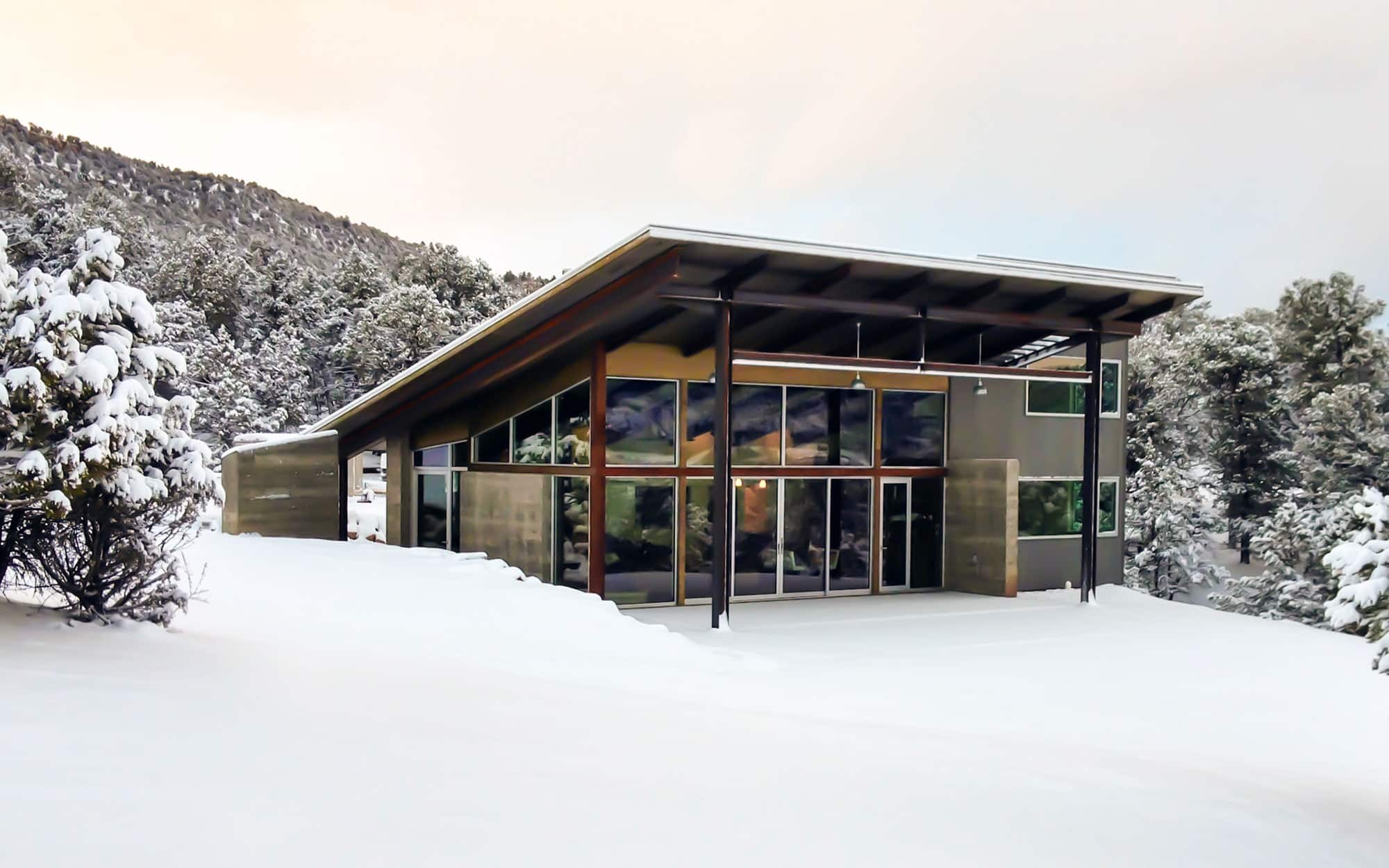 A home with a nearly all glass façade in a snowy landscape.