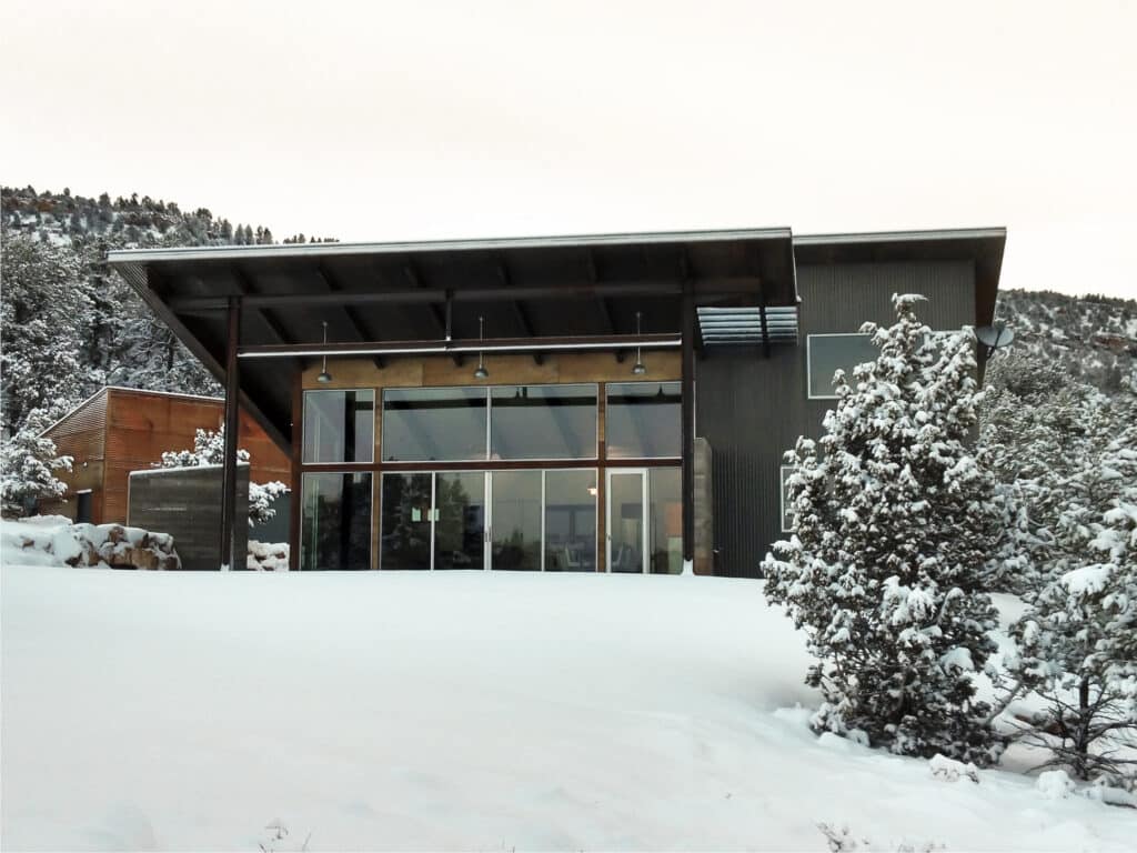 A house with an all-glass facade sits on a mountainside surrounded by snow.