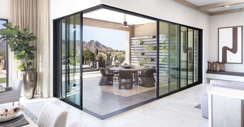 A 90-degree multi-slide glass door is open, revealing an outdoor seating area that faces a mountain.