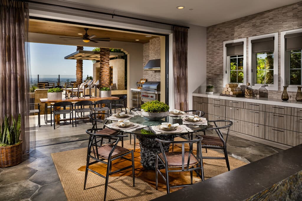 An indoor dining area is seamlessly connected to an outdoor cooking space by a pocketing multi-slide glass door.