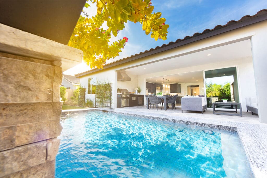 An outdoor pool is directly available from an open multi-slide glass door transitioning from the kitchen and living room.