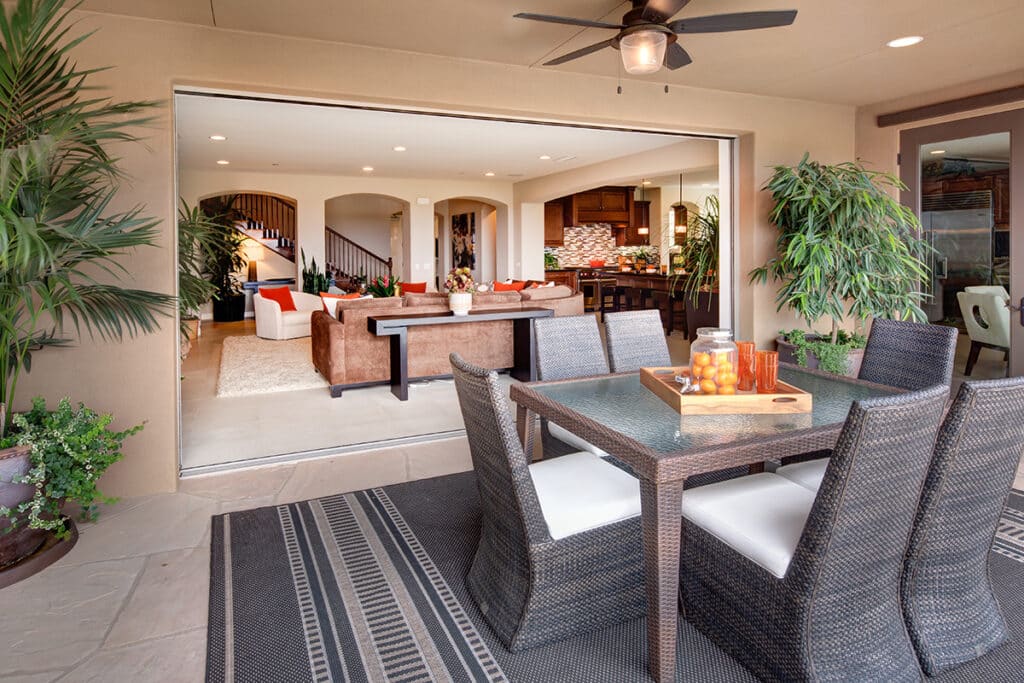 An open multi-slide glass door connects an indoor living room with an outdoor dining area.