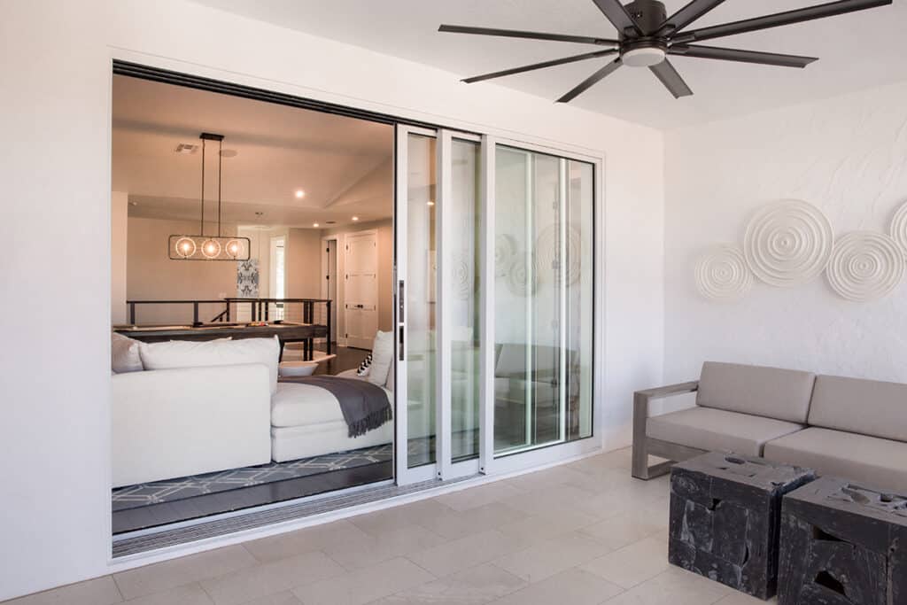 A covered outdoor seating area reaches the indoor living room through a partially opened multi-slide glass door.