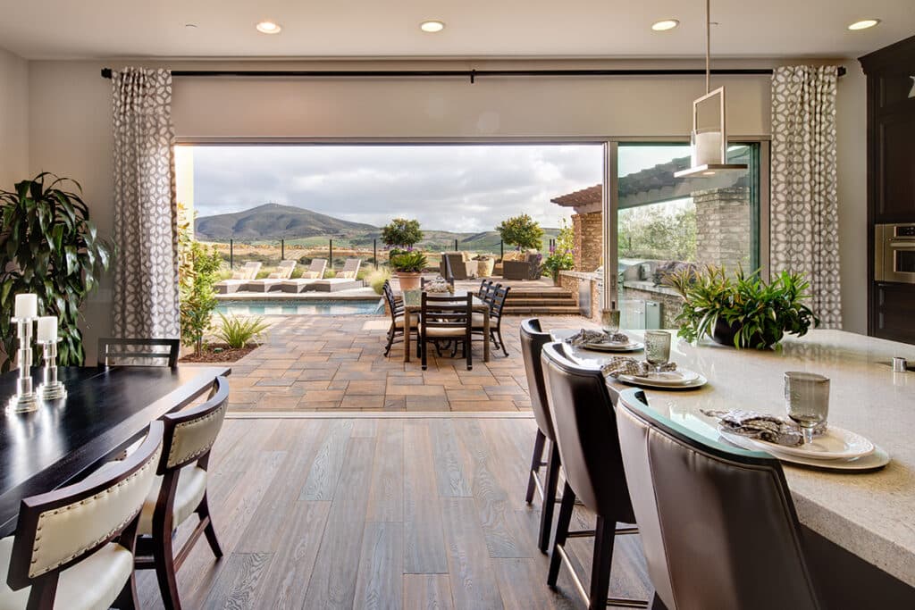 An indoor dining room connects to a mountain landscape view via moving walls of glass.