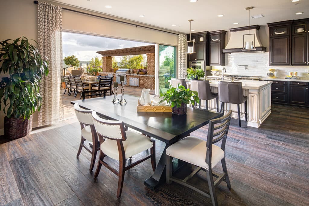 An indoor kitchen and dining space expands to an outdoor dining and grilling area through an open multi-slide glass door.