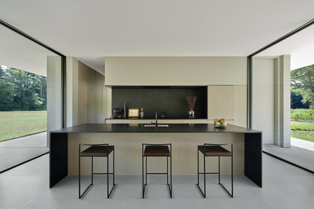 A streamlined modern kitchen island with waterfall edge sits between two large open doorways.