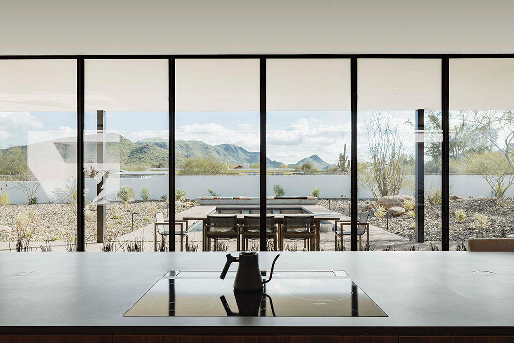 A floor-to-ceiling multi-slide door connects this Arizona home’s kitchen to the backyard with mountainous views.