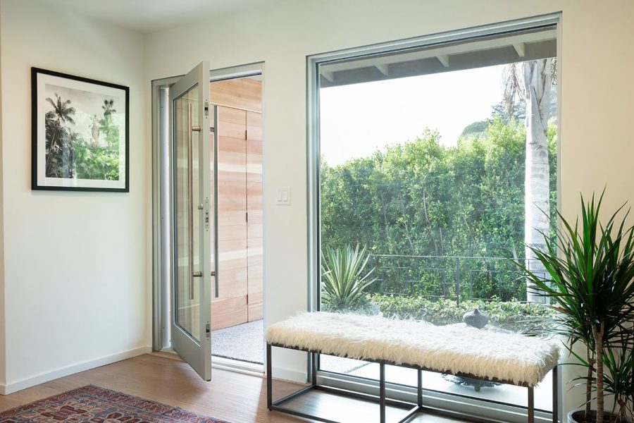 An aluminum pivot door next to a large, fixed window look out to a lush front yard.