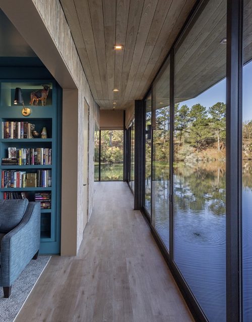 A vibrant library shares a long glass wall with the hallway, with the lake visible outside.