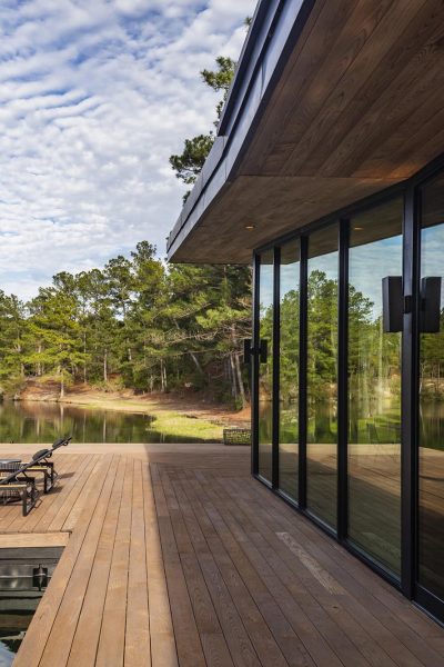 A wall of closed multi-slide glass doors reflect a lakeside view surrounding the home.
