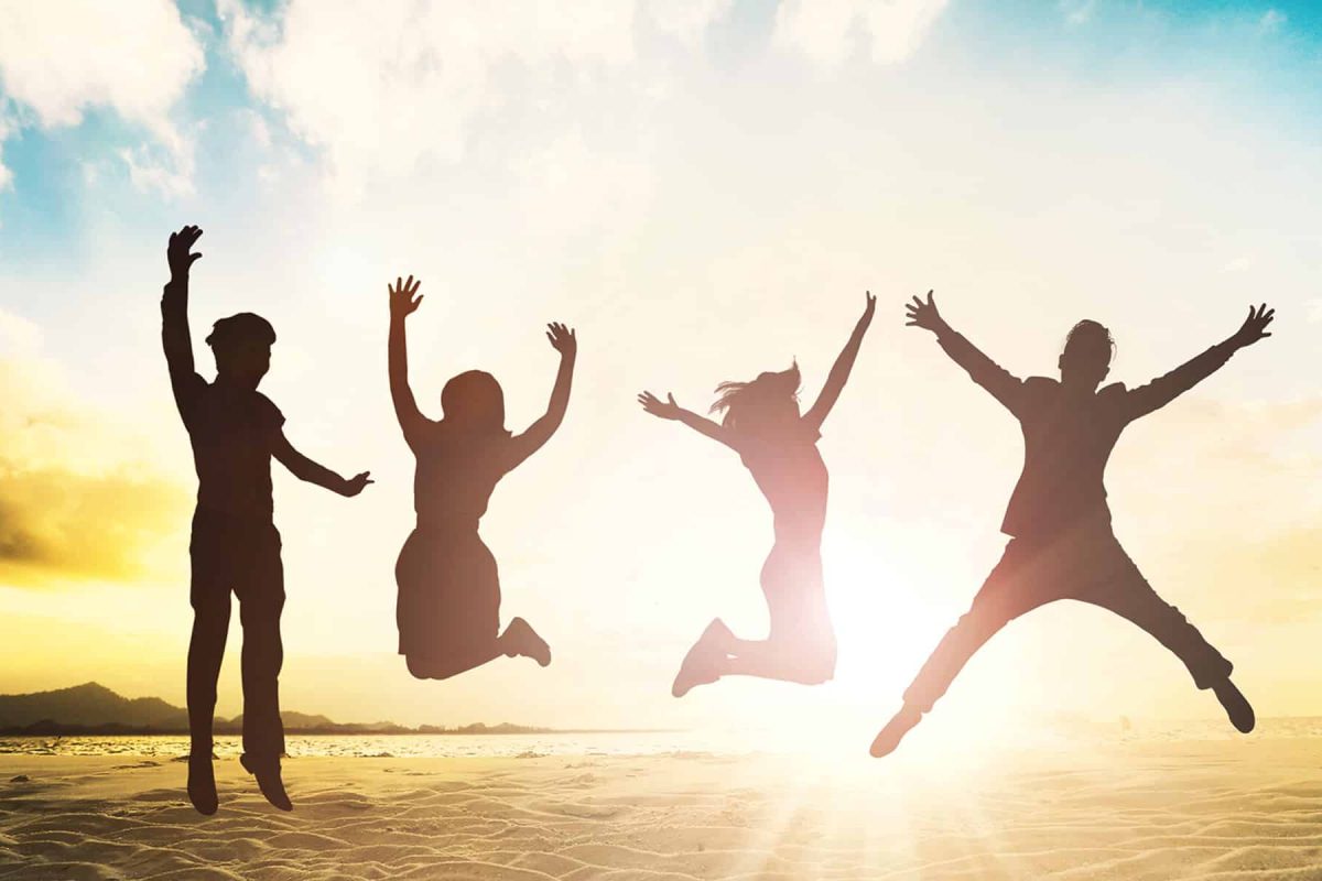 An image of four people jumping on a beach with the sun behind them.