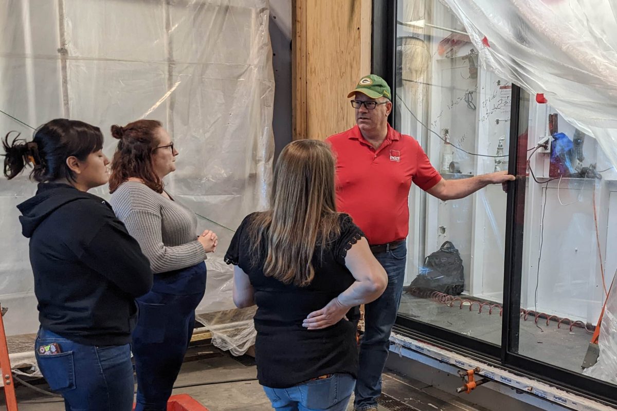A man is presenting to three women in front of a multi-slide door.