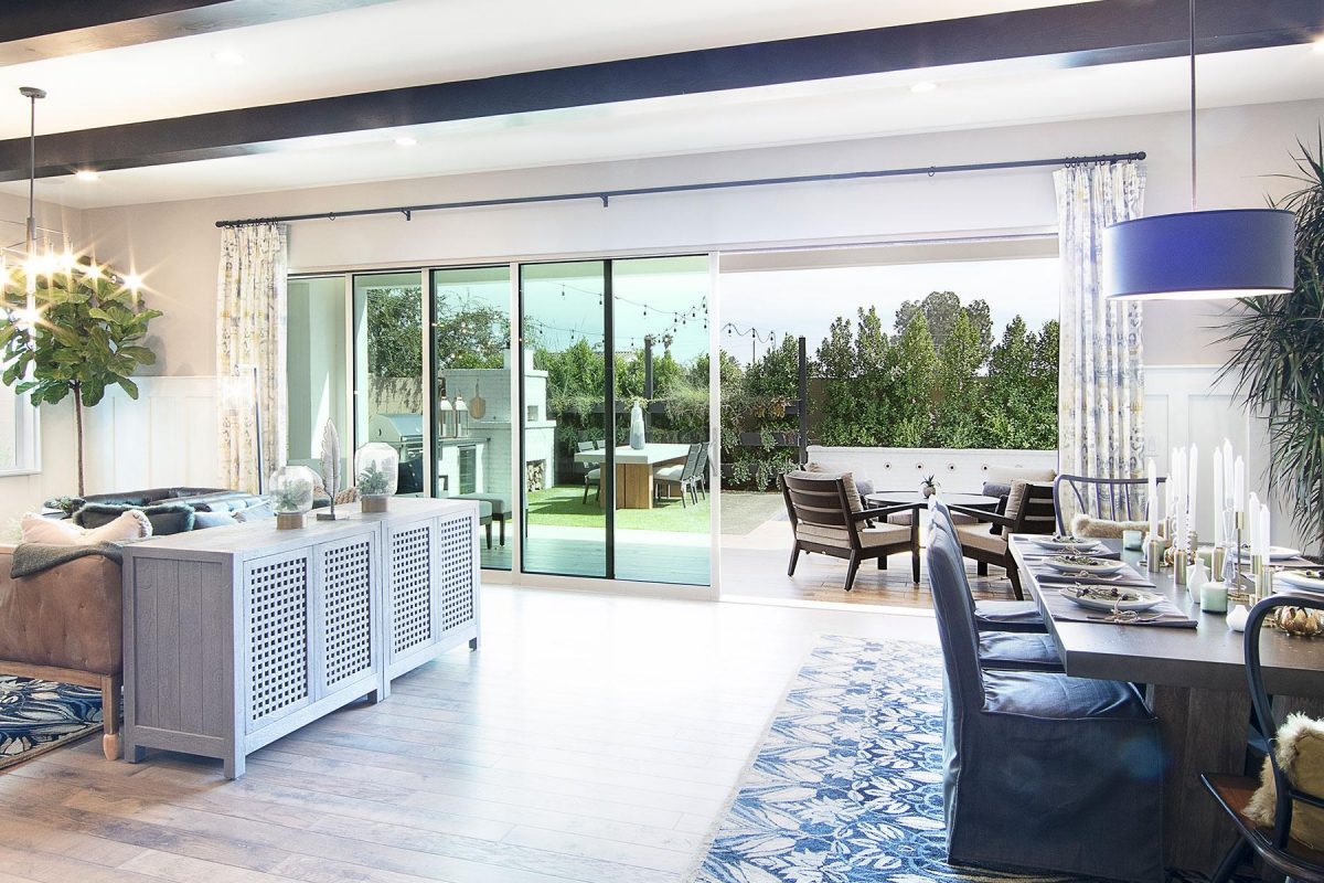 An indoor living and dining room seamlessly transitions to a backyard living space through a multi-slide glass door.